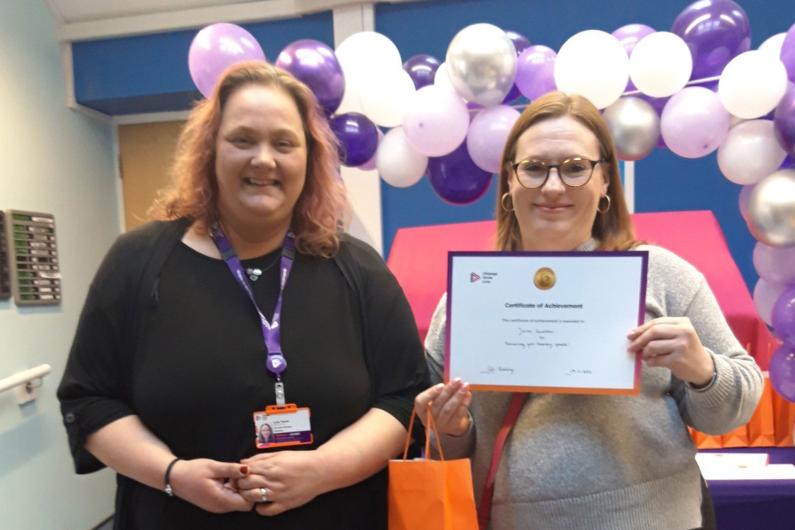 Someone receiving a certificate at our Reading service. There is a balloon arch behind them!