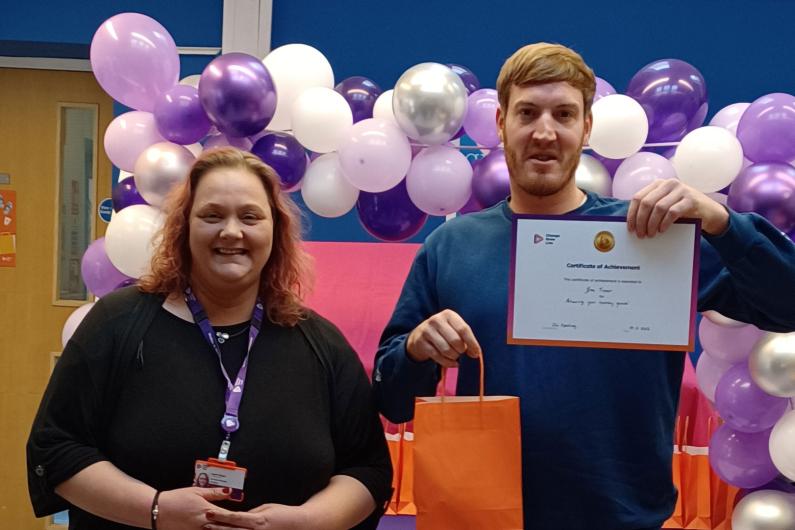 Someone receiving a certificate at our Reading service. There is a balloon arch behind them!
